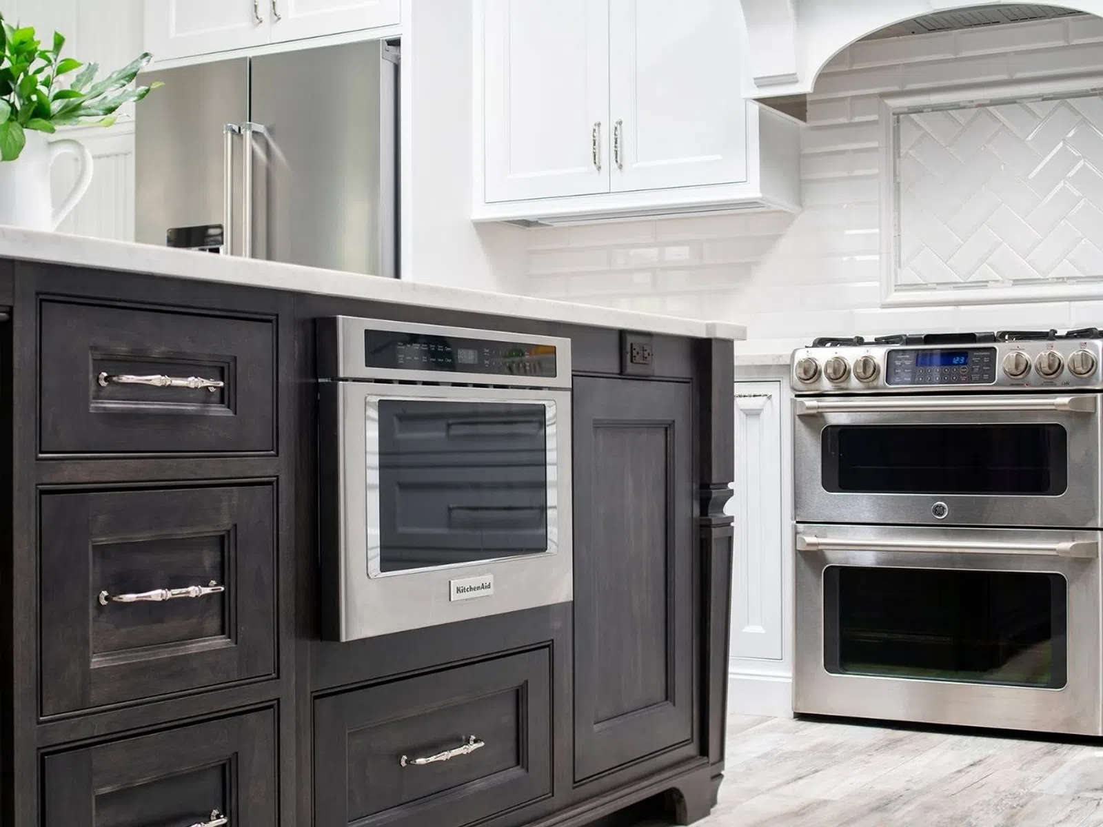 Modern kitchen with dark island, built-in stainless steel microwave, stainless steel stove, white cabinetry, and tiled backsplash.