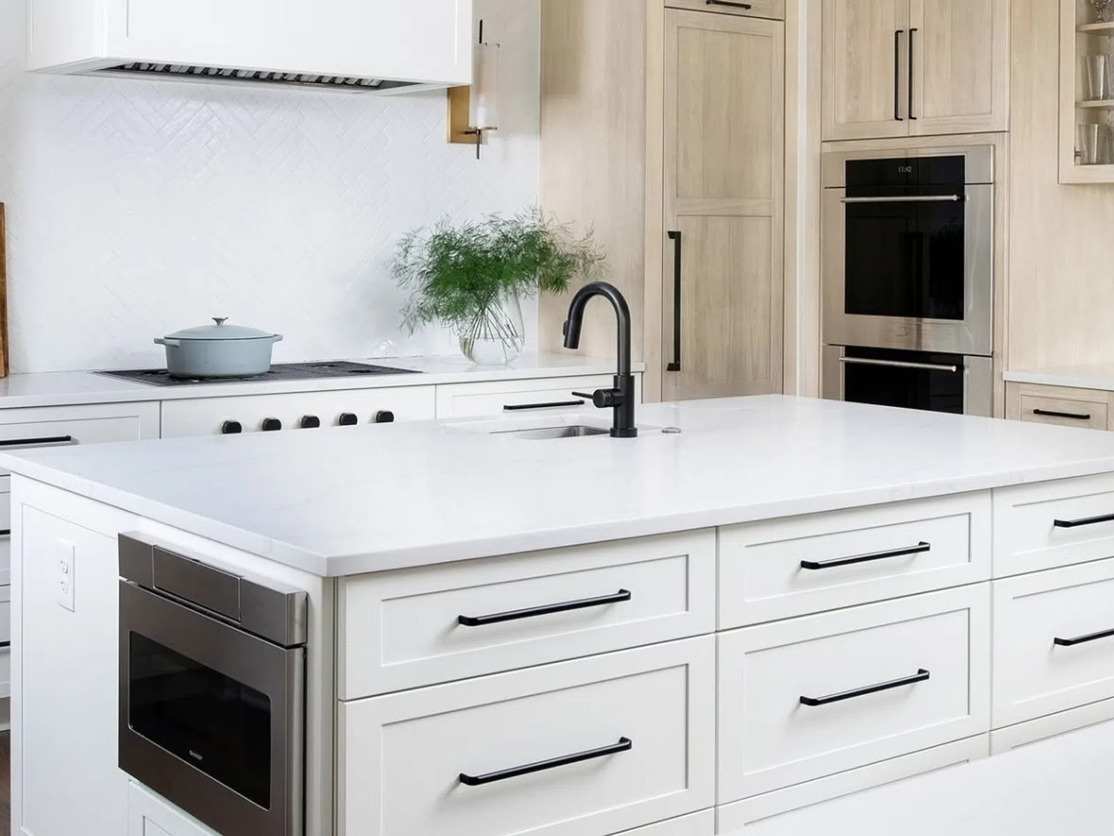 Modern white kitchen with large island, black hardware, built-in appliances, and minimalist decor.
