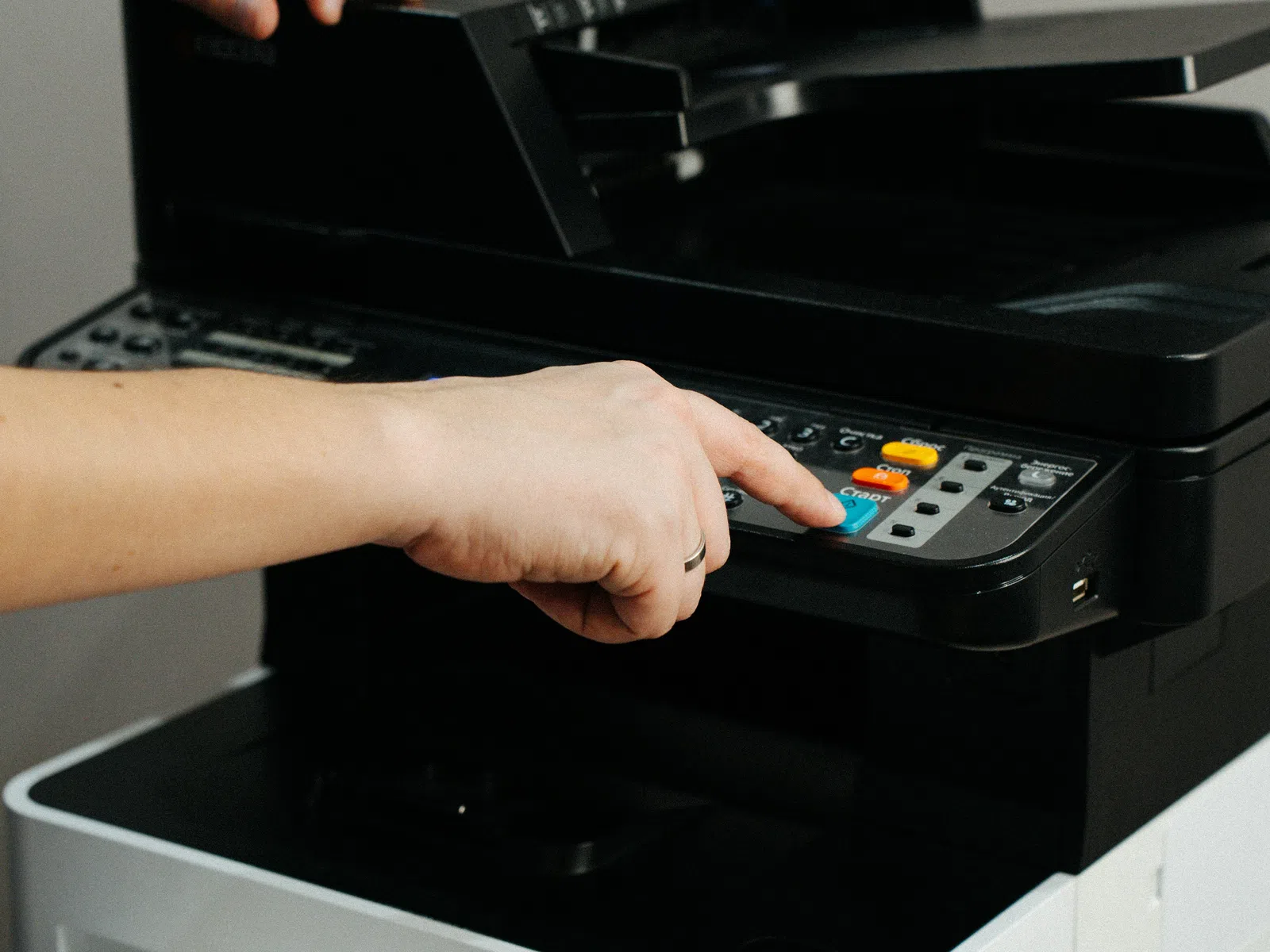 Person using a multifunction printer pressing copy button to start scanning or printing documents.