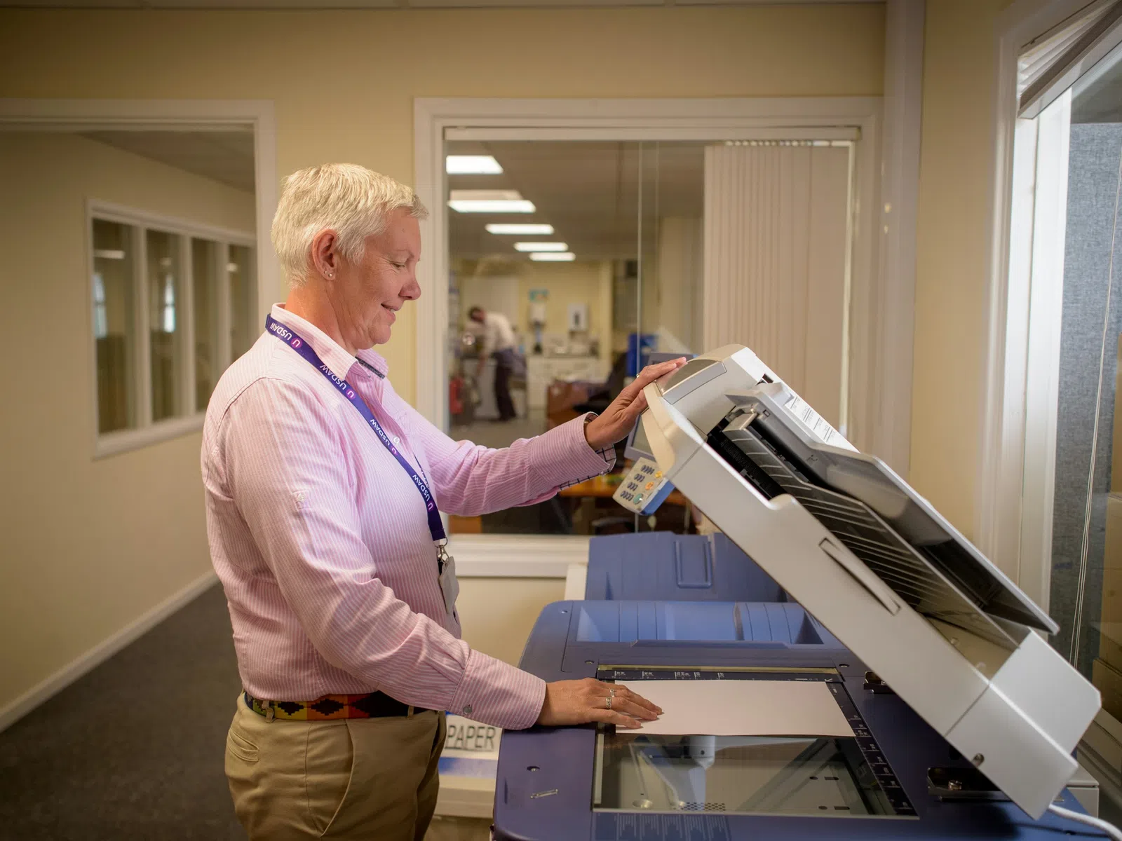 Man in pink shirt using a large office photocopier inside a brightly lit office room