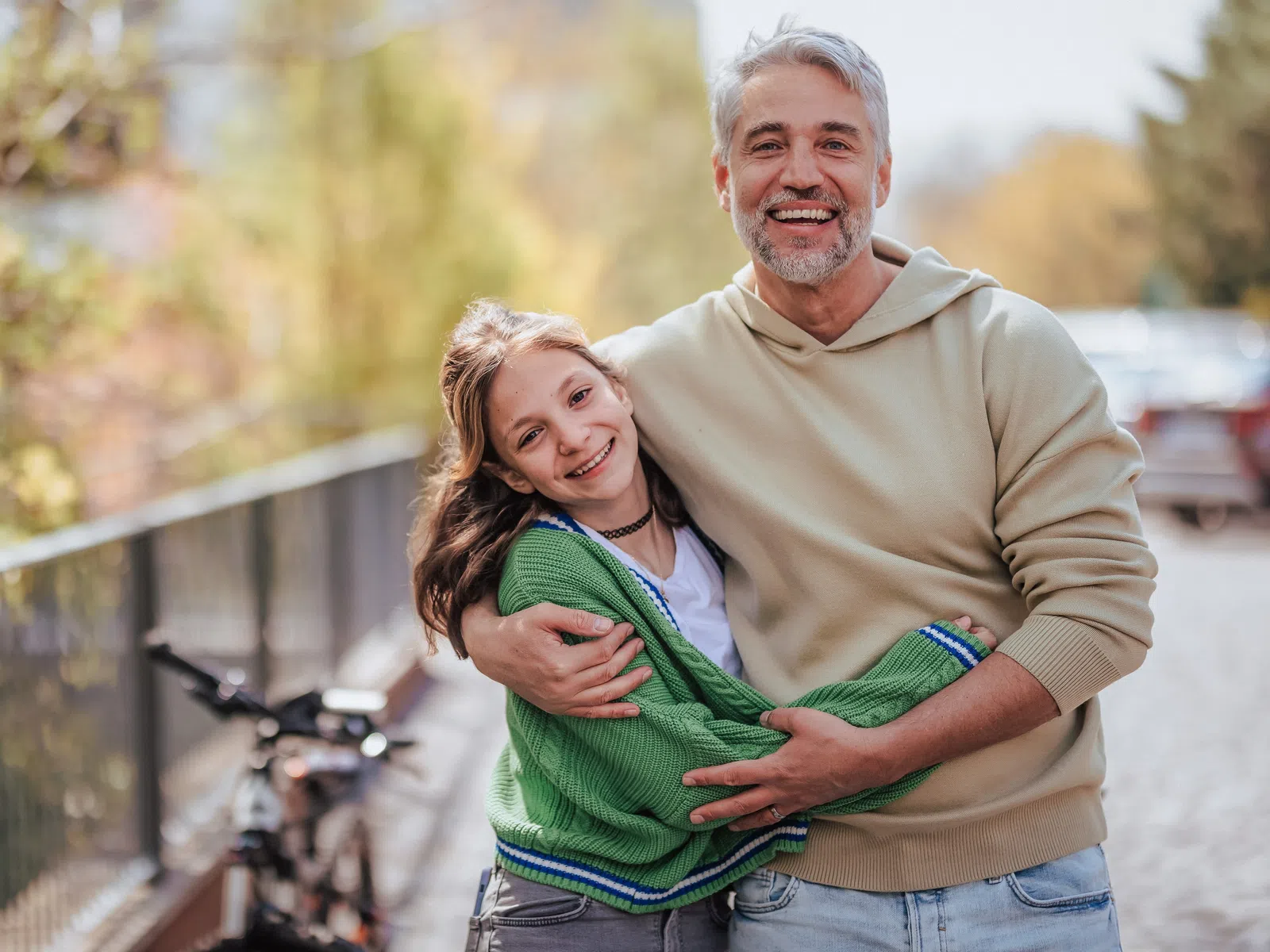 Smiling father hugging daughter outdoors on a sunny day with bicycle in the background