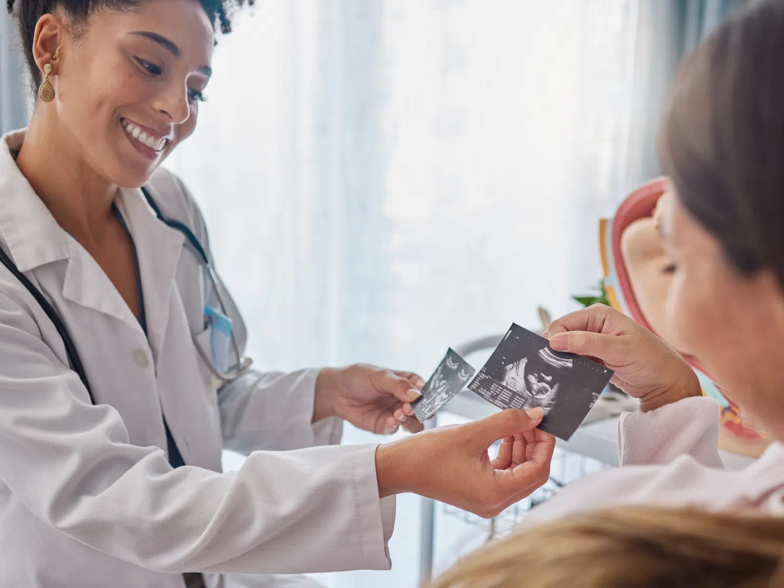 Smiling female doctor showing ultrasound images to pregnant woman in medical office with natural light