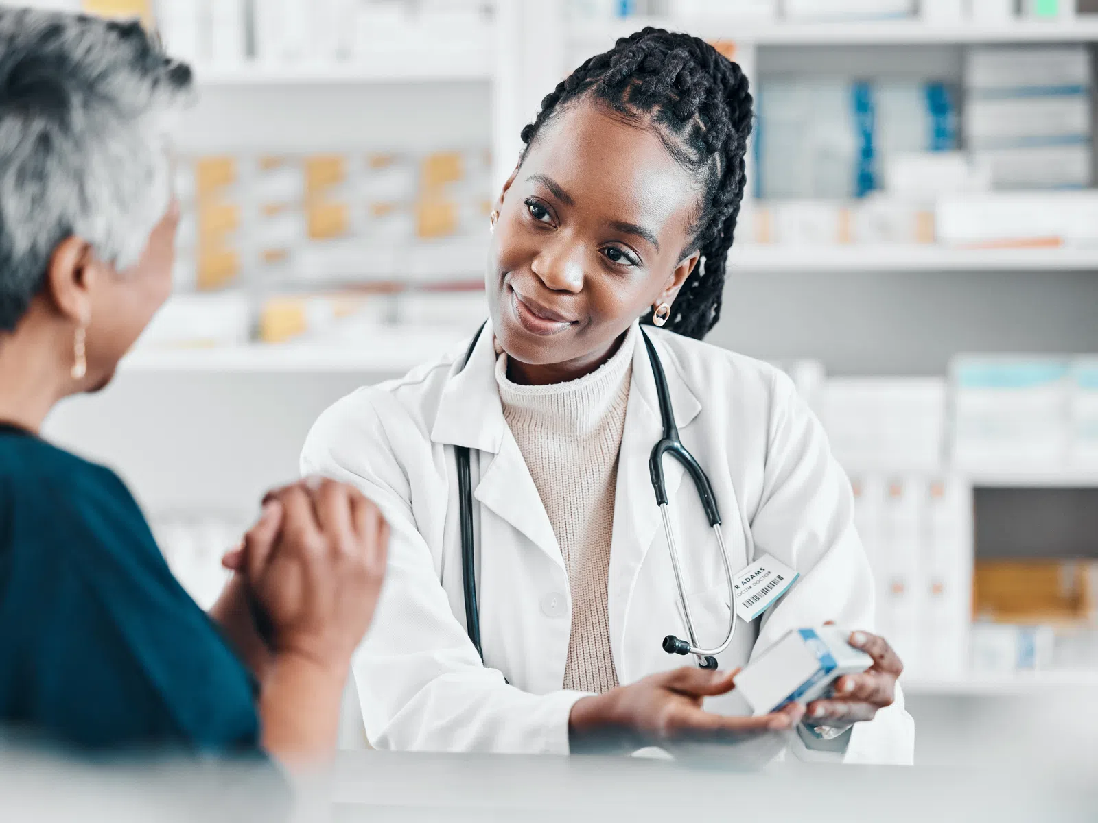 Female pharmacist in a white coat explaining medication to an elderly woman in a pharmacy setting.