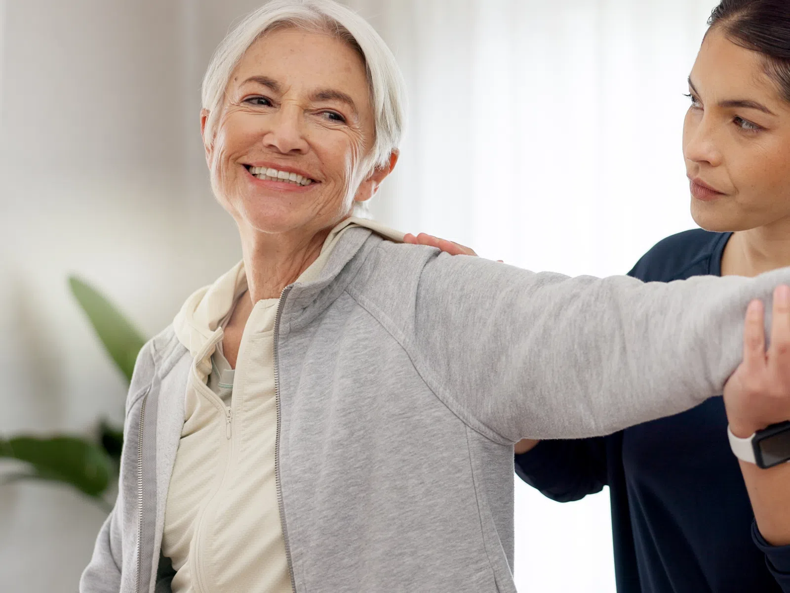Senior woman exercises assisted by a physical therapist in a bright indoor setting.