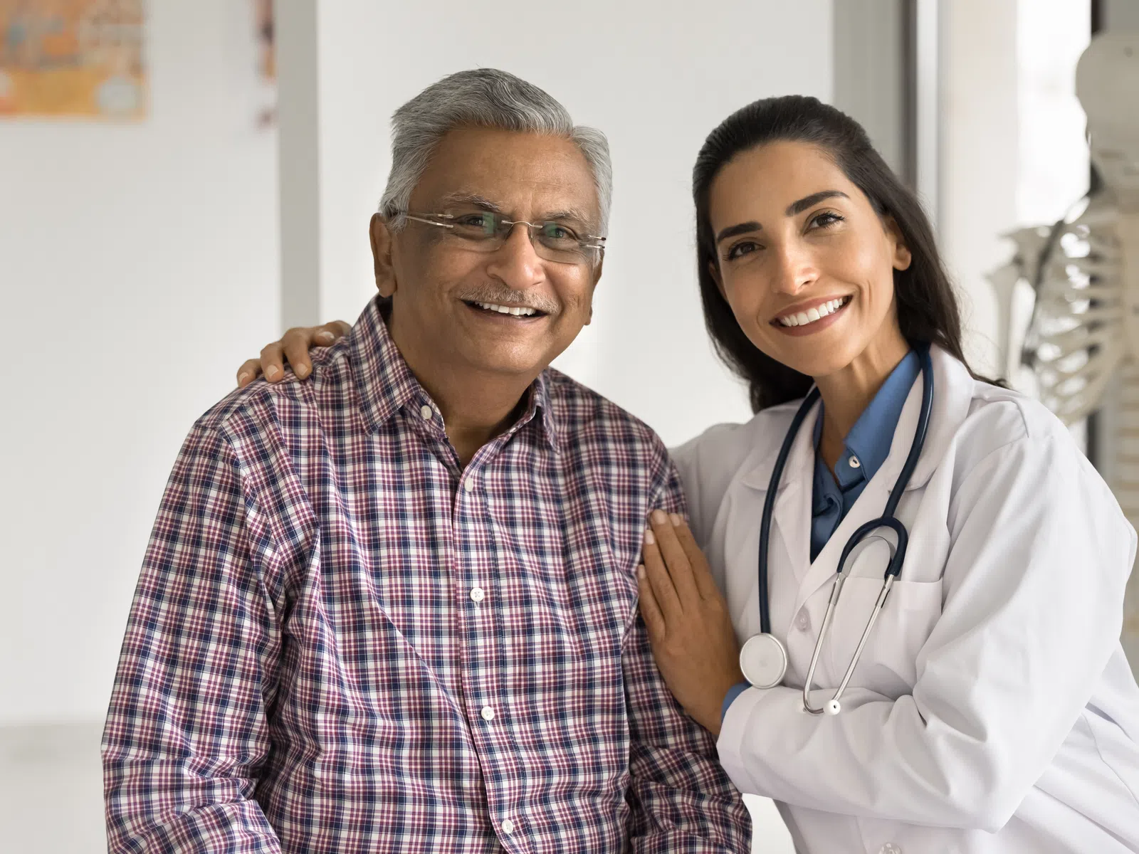 Smiling female doctor with stethoscope embraces senior male patient in medical office with skeleton model.