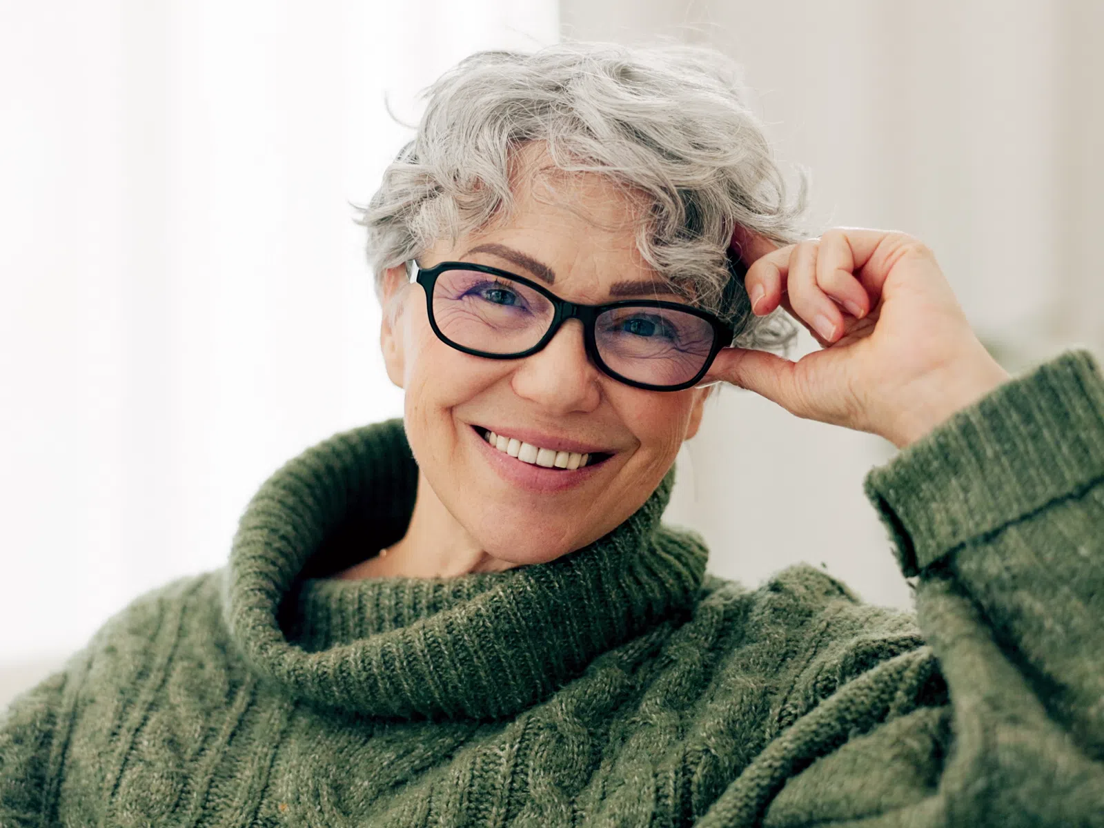 Smiling elderly woman with short gray hair and glasses wearing a green knitted sweater indoors