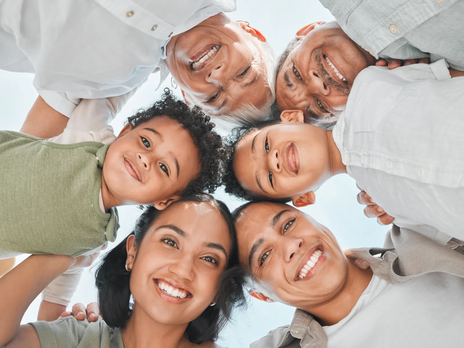 Smiling multi-generational family in a circle looking down at the camera against a clear sky.