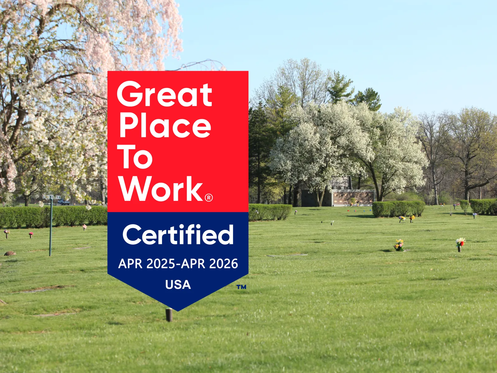 Great Place to Work Certified badge displayed on a green lawn with trees and flowers on a sunny day