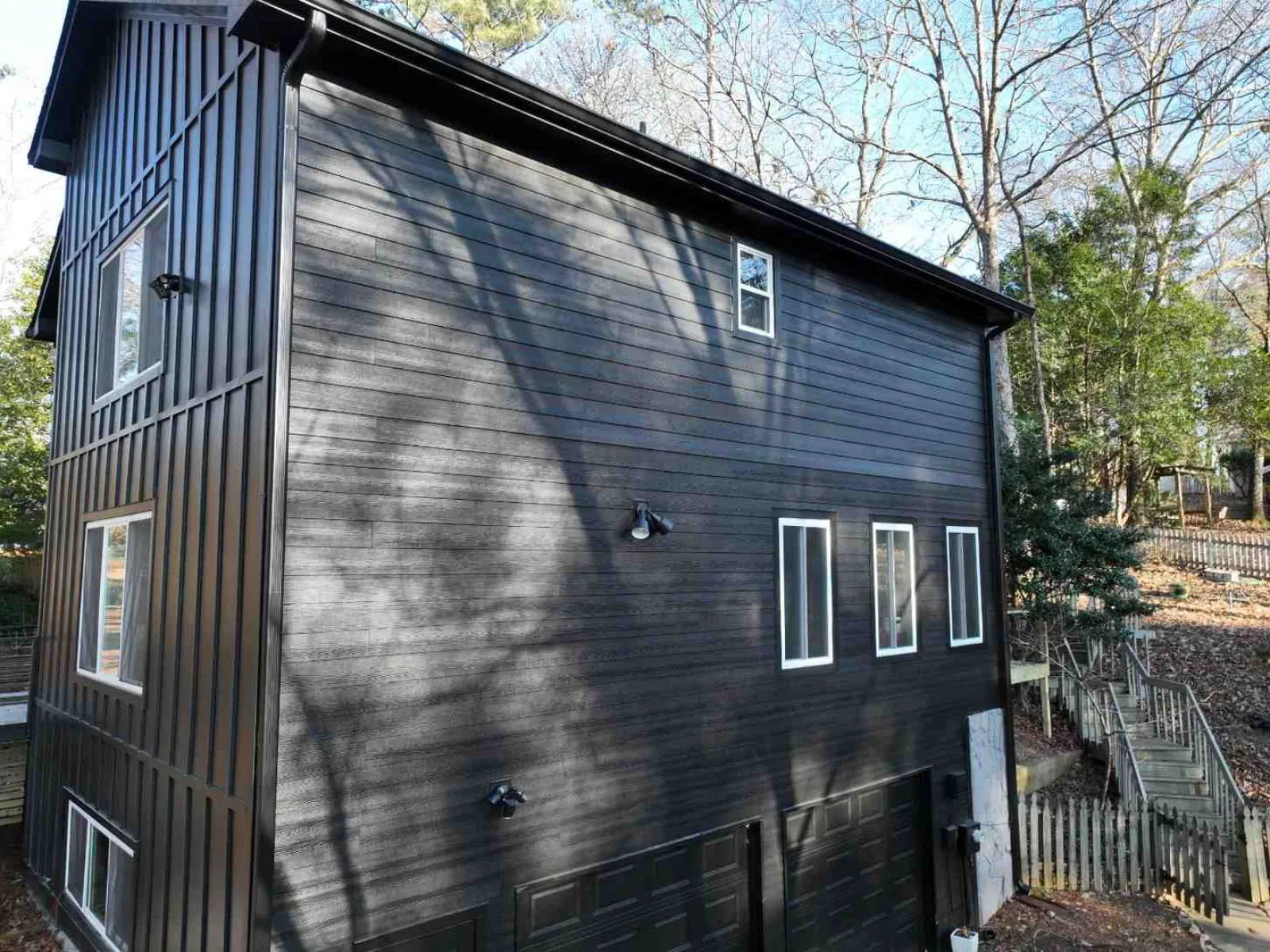 Modern black house exterior with vertical and horizontal siding, white windows, and surrounding trees
