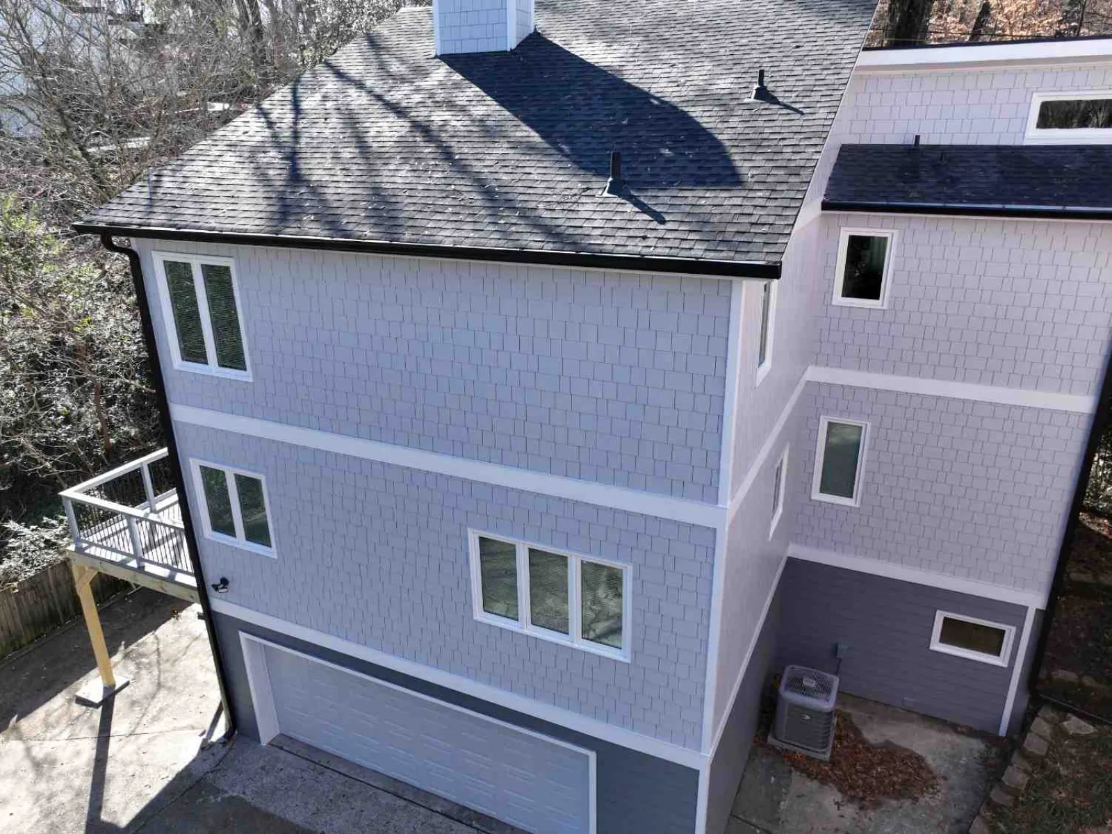 Modern two-story house with gray shingles, white trim, multiple windows, and attached garage in sunny setting.