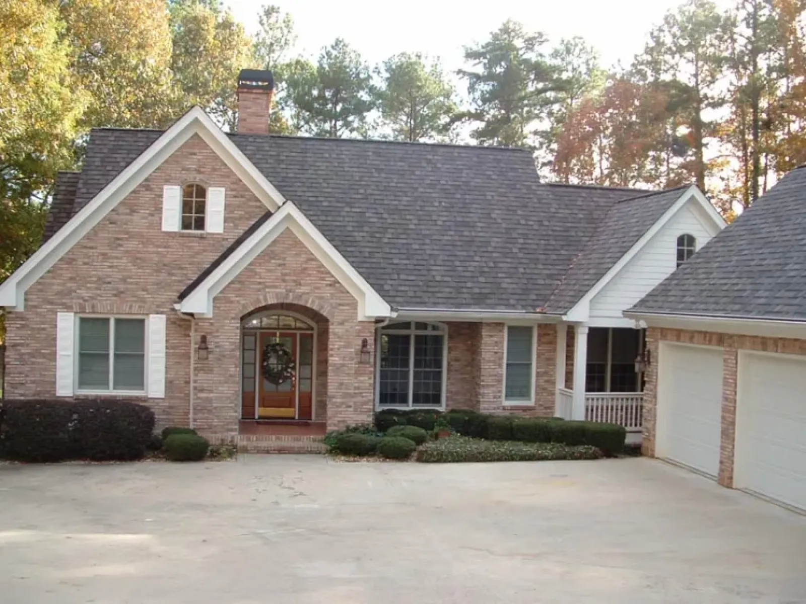 Front view of a brick suburban house with a gable roof, white shutters, and an attached garage surrounded by trees.