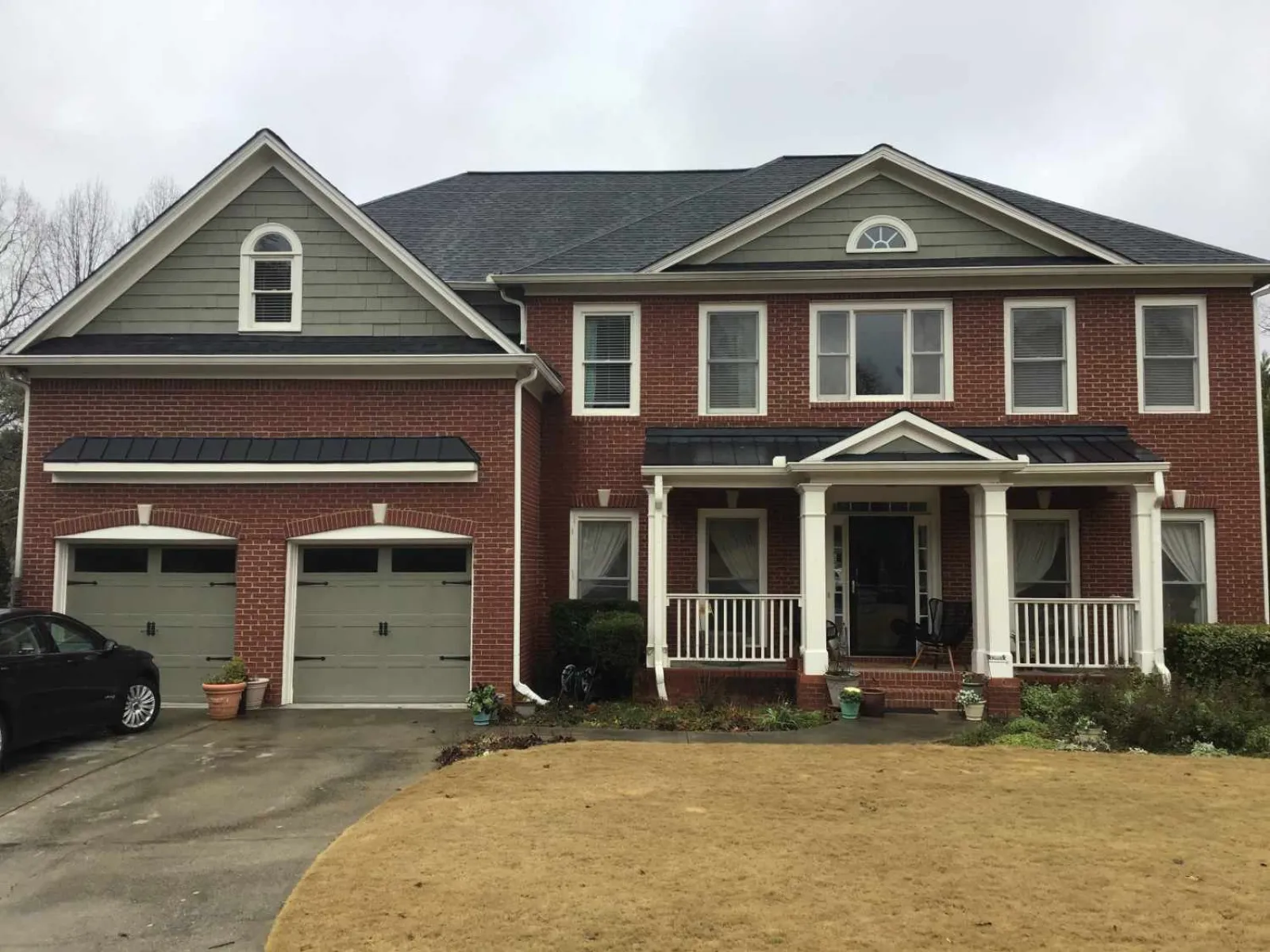 Two-story brick house with gray roof, double garage, white porch columns, and a lawn in front on a cloudy day