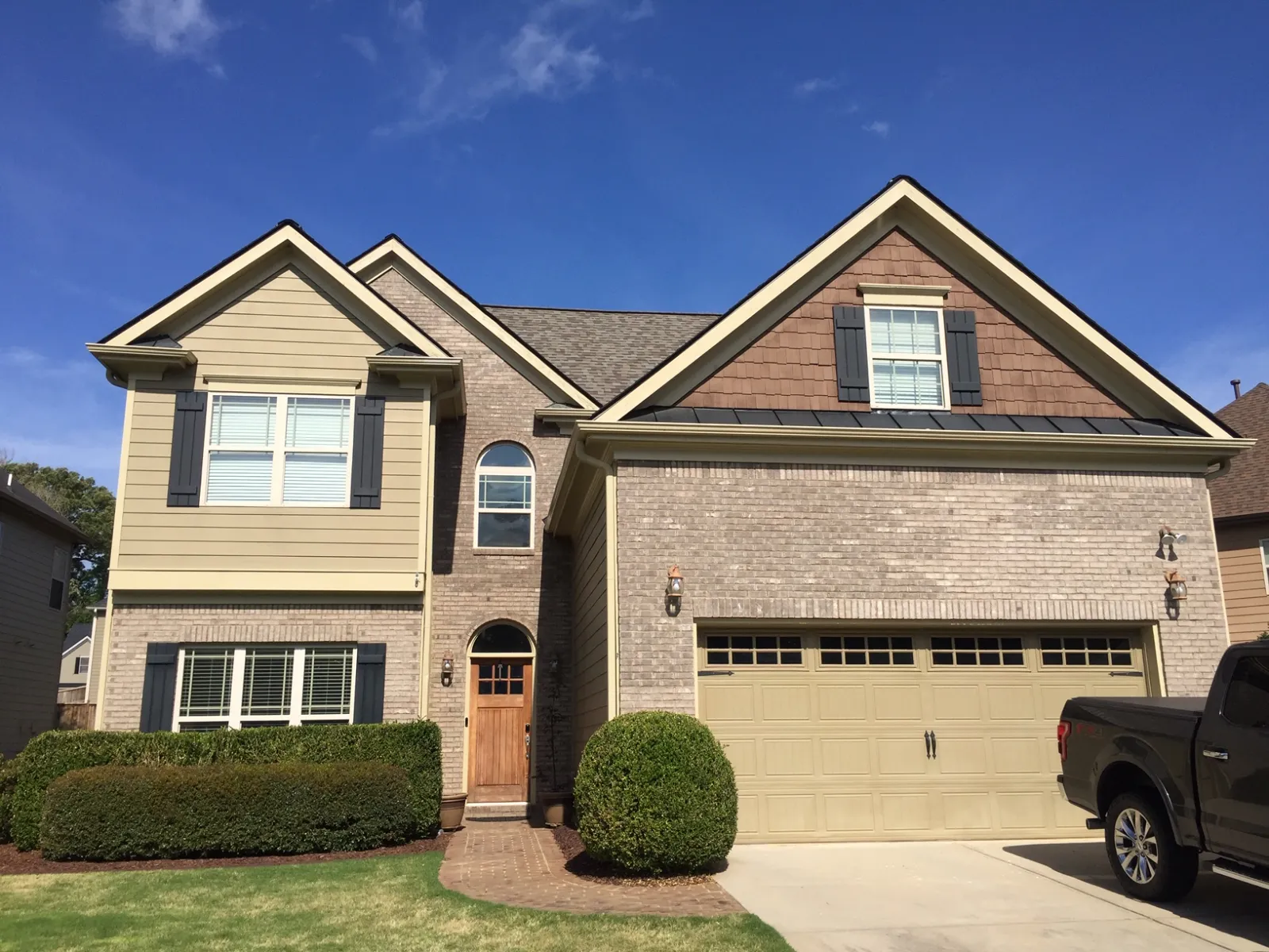 Modern two-story suburban house with beige brick exterior, large windows, green lawn, and attached garage on sunny day