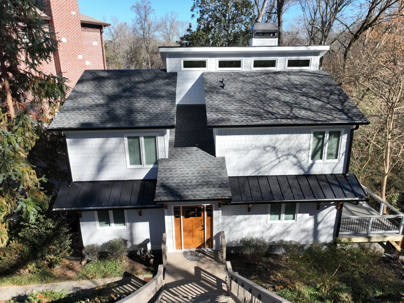 Aerial view of a modern gray home surrounded by trees, featuring a stylish black roof and inviting entrance.