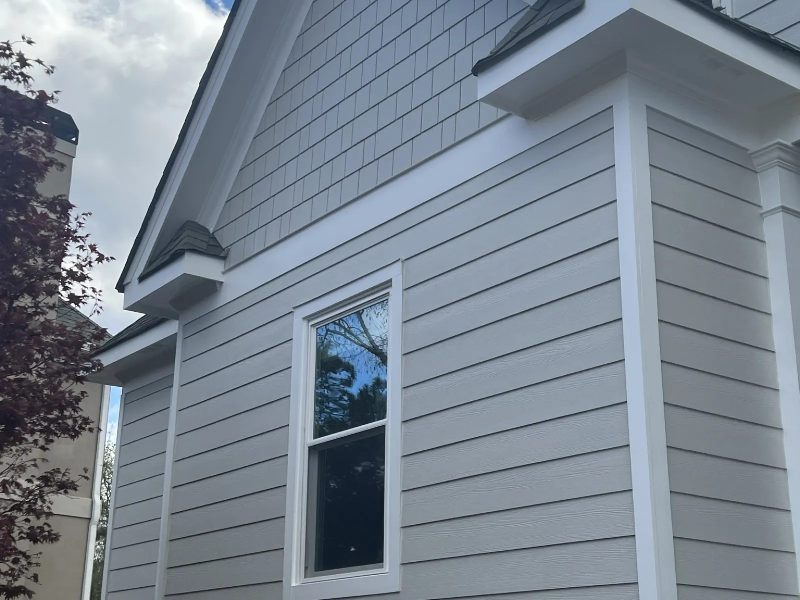 Gray and white modern house exterior with siding, stone foundation, single window, and blue sky with clouds.
