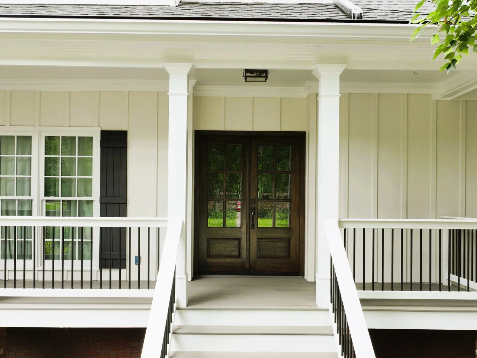 Charming modern house entrance with double doors, white columns, and lush green surroundings.