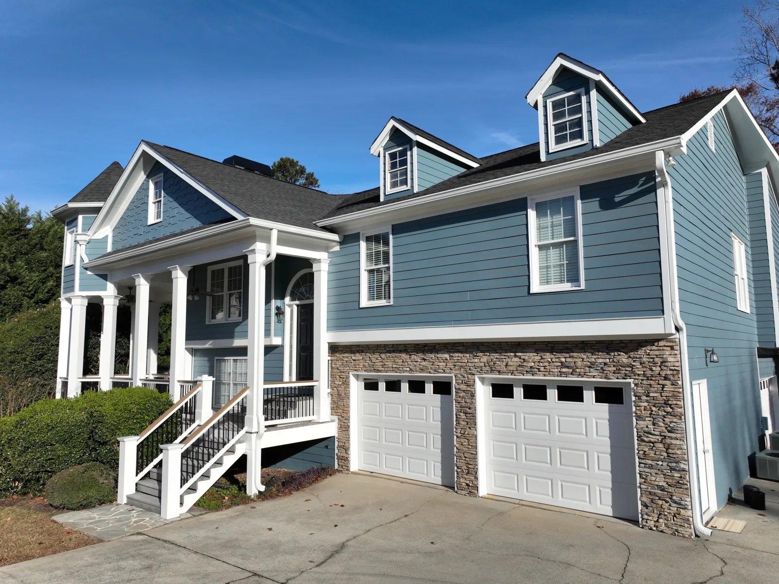 Elegant blue house with stone accents, white pillars, and double garage under a clear blue sky.