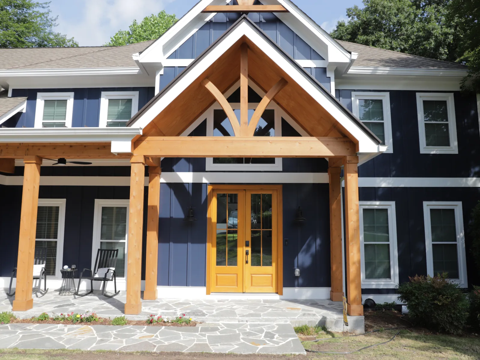 Modern blue house exterior showcasing a wooden porch with tall peaked roof and stylish entrance.