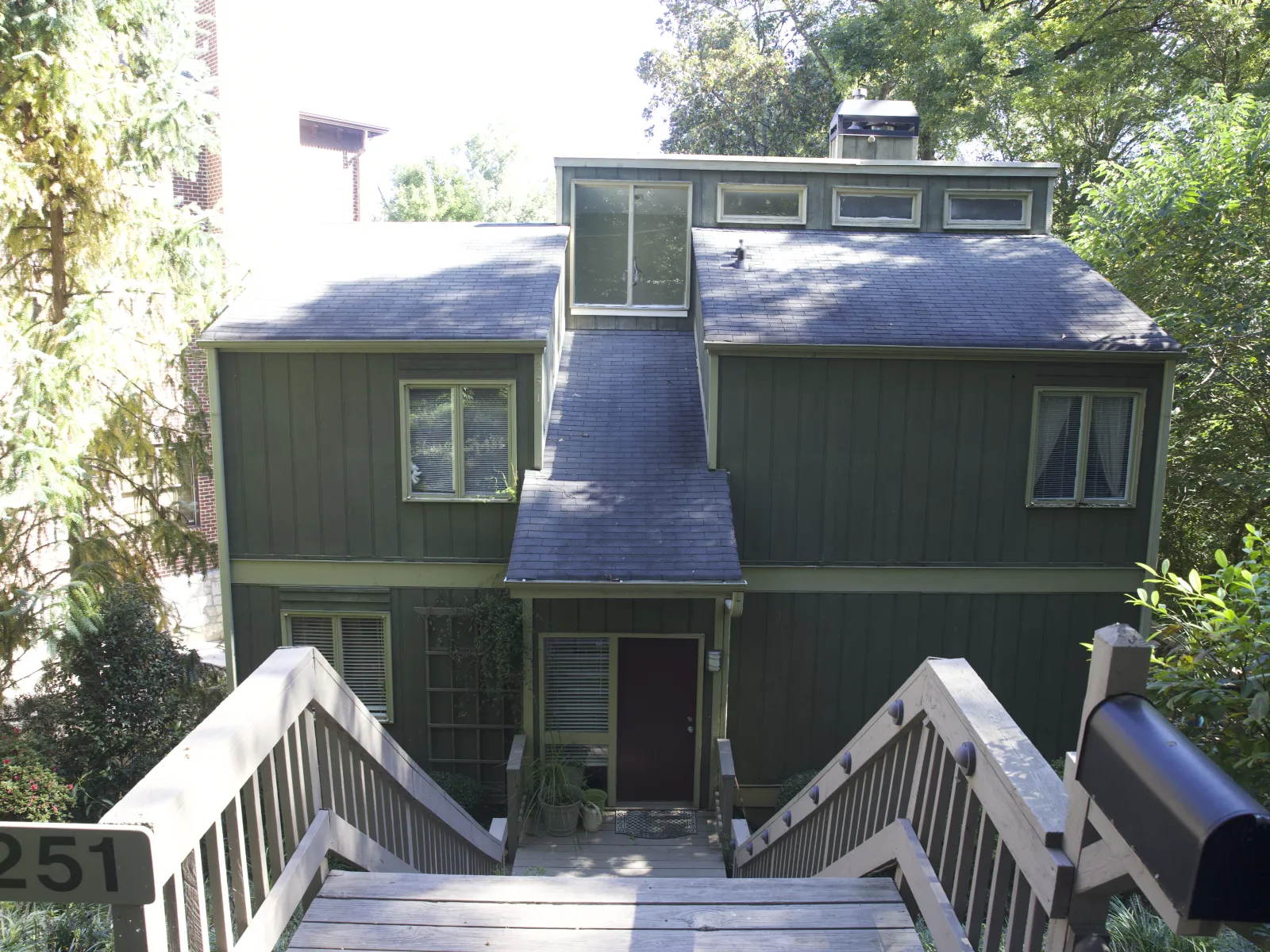 Charming green house with a sloped roof, surrounded by greenery and steps leading to the front door.