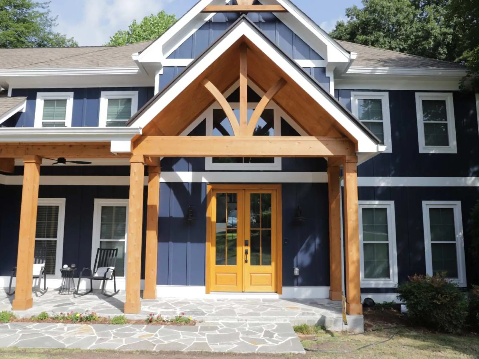 Modern blue house with wooden porch structure and yellow double front doors under clear sky