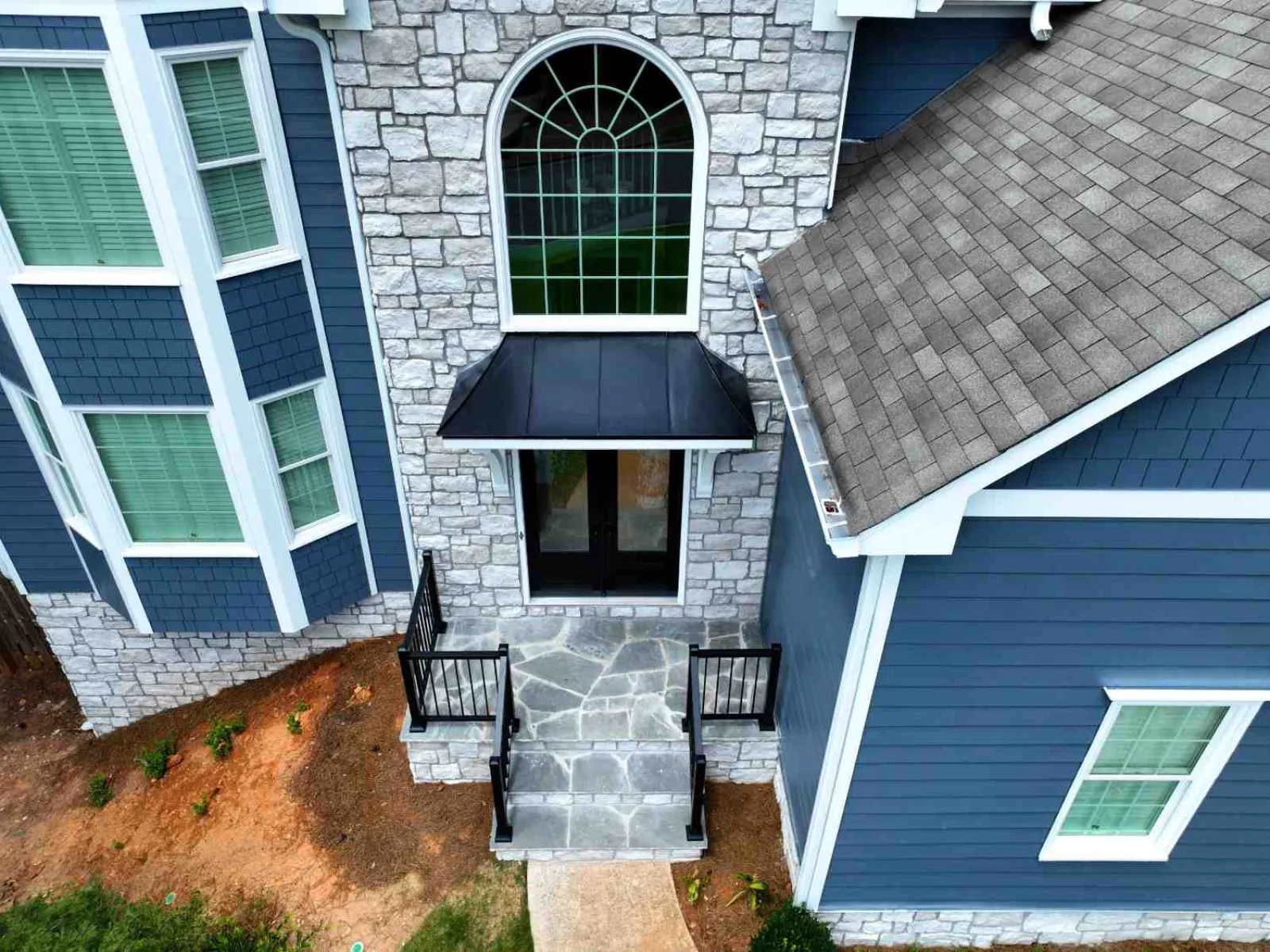 Front entrance of a blue house with stone facade, large arched window, and black metal awning above door.