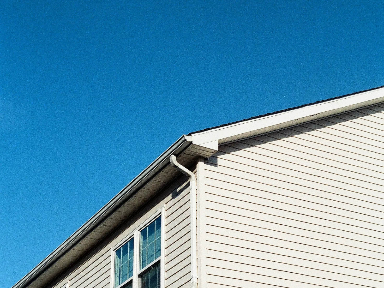 Light beige residential house siding with windows and clear blue sky in the background