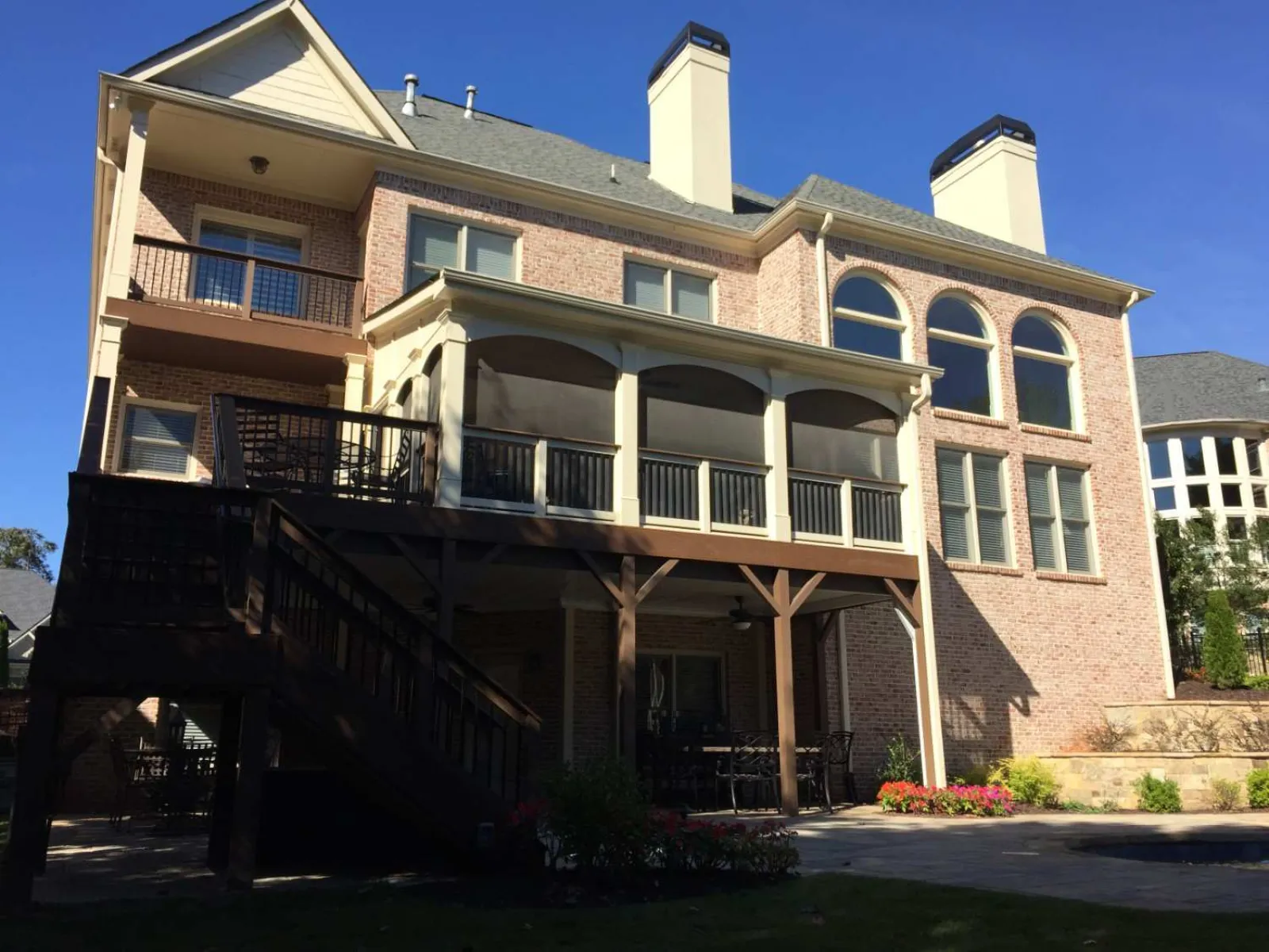 Large brick house with two chimneys, arched windows, covered balcony, and outdoor staircase under blue sky