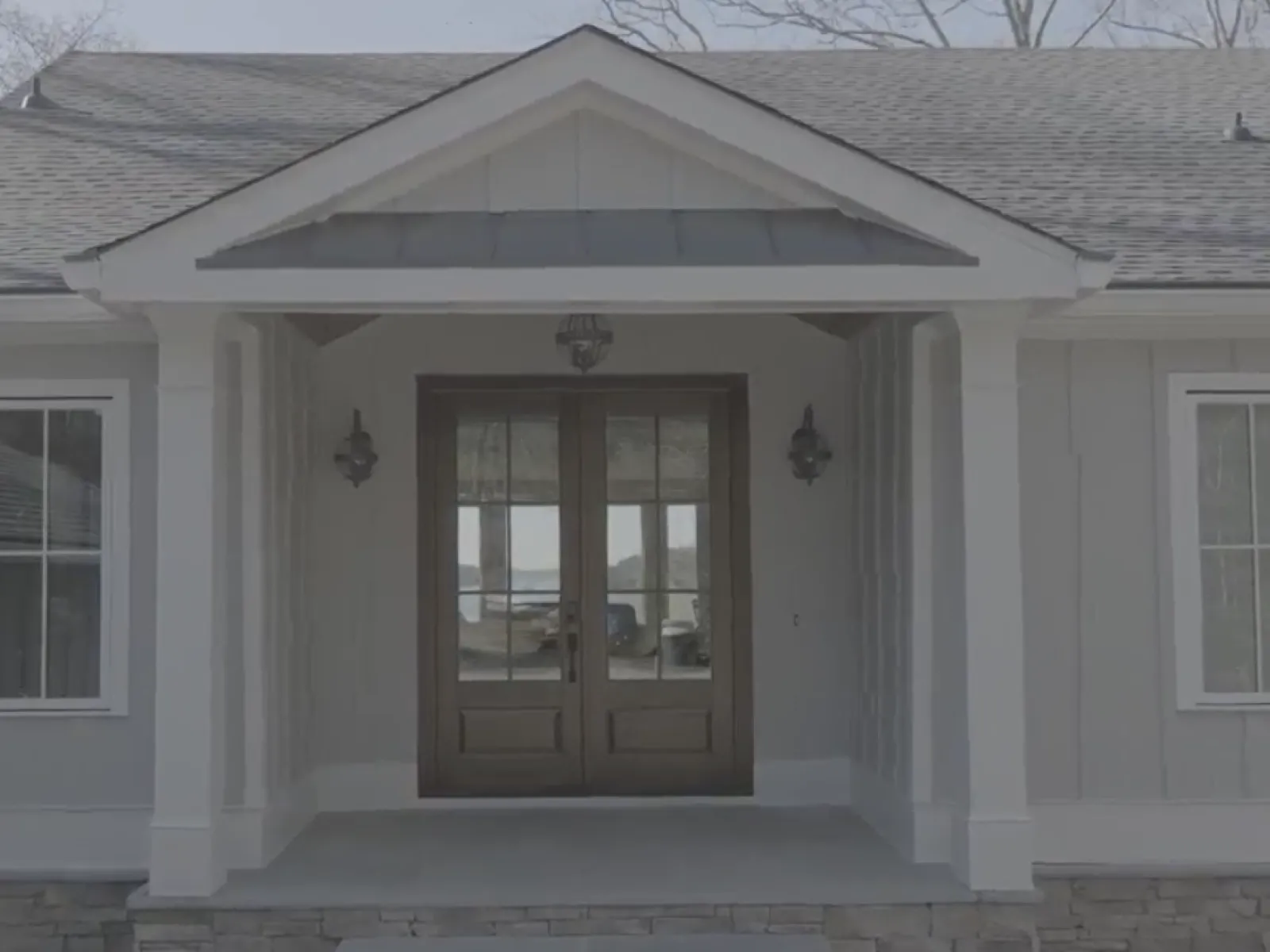 Front view of a modern house entrance with double wooden doors and two side windows under a covered porch.