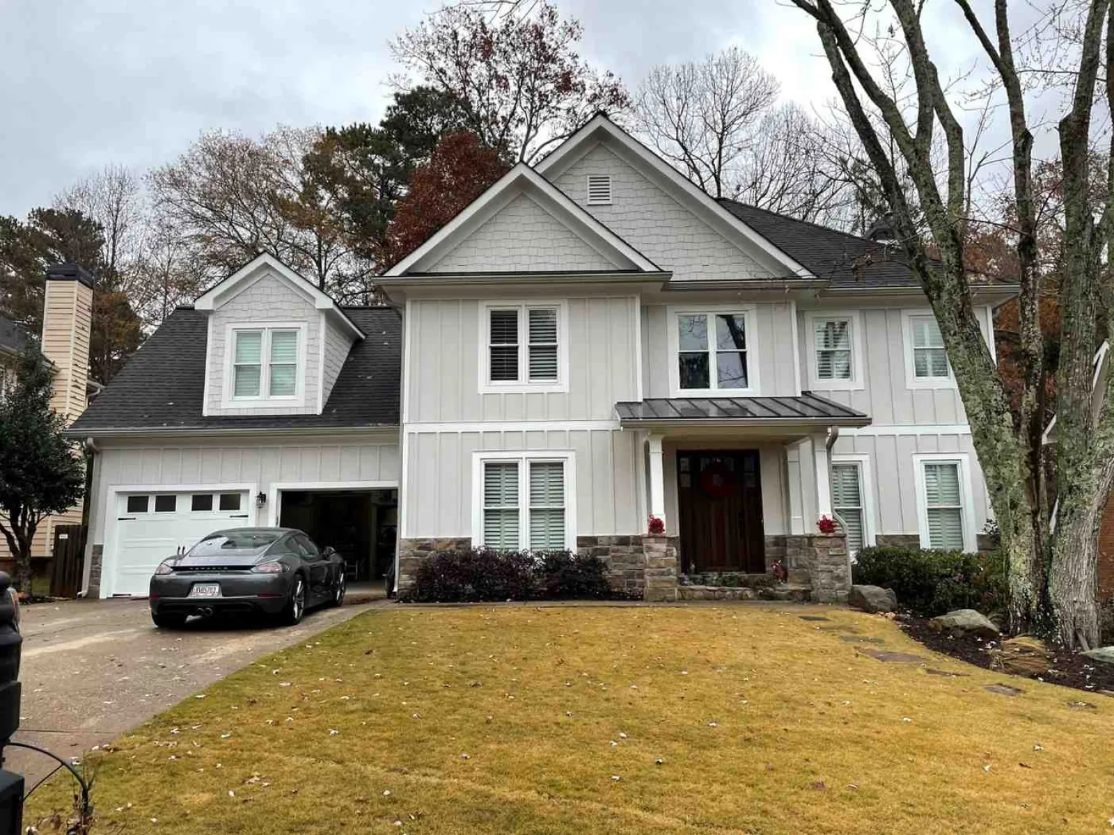 Two-story white house with stone accents, a front porch, attached garage, and a black car parked outside on a cloudy day