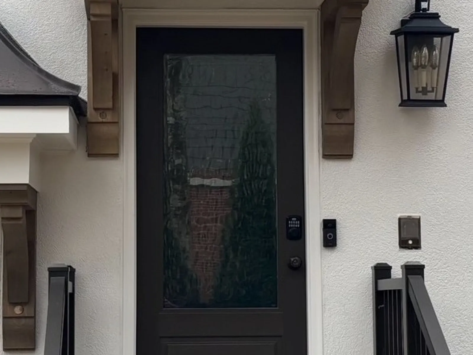 Modern black front door with textured glass panel, gray stone steps, black railing, and exterior lantern light.