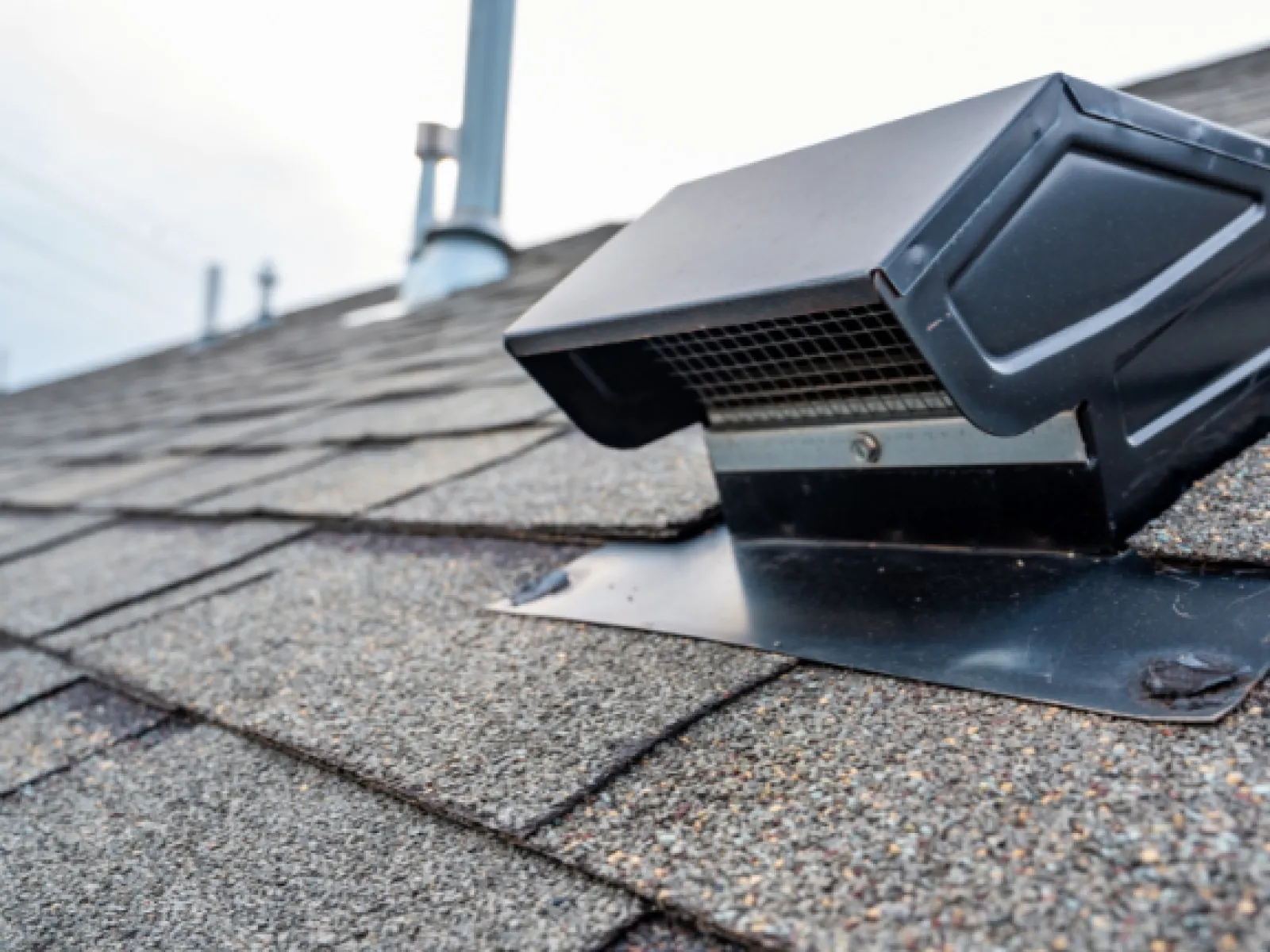 Black roof vent installed on asphalt shingle roof under a cloudy sky for attic ventilation.