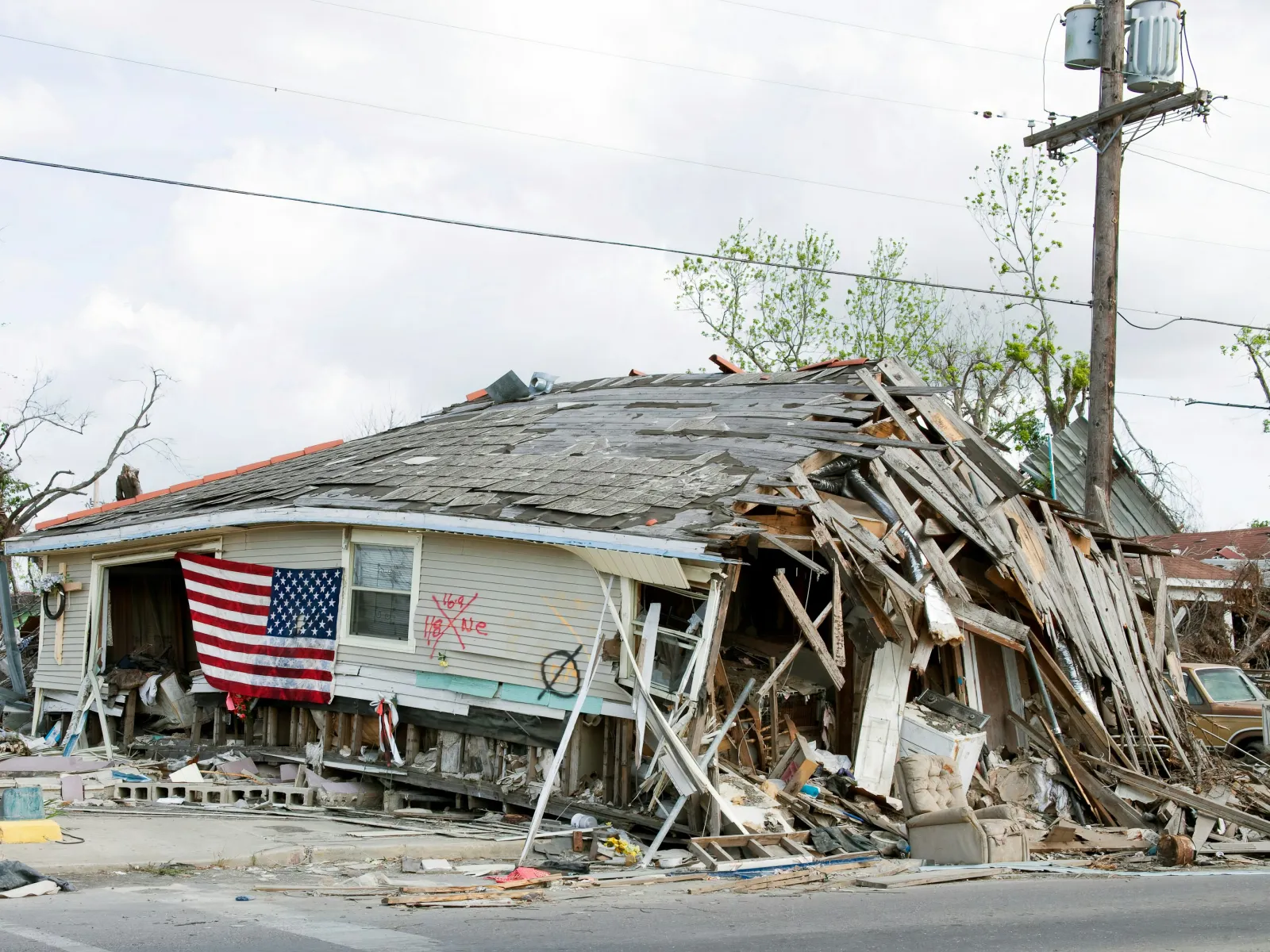 Severely damaged house collapsed with an American flag hanging on the side after a natural disaster