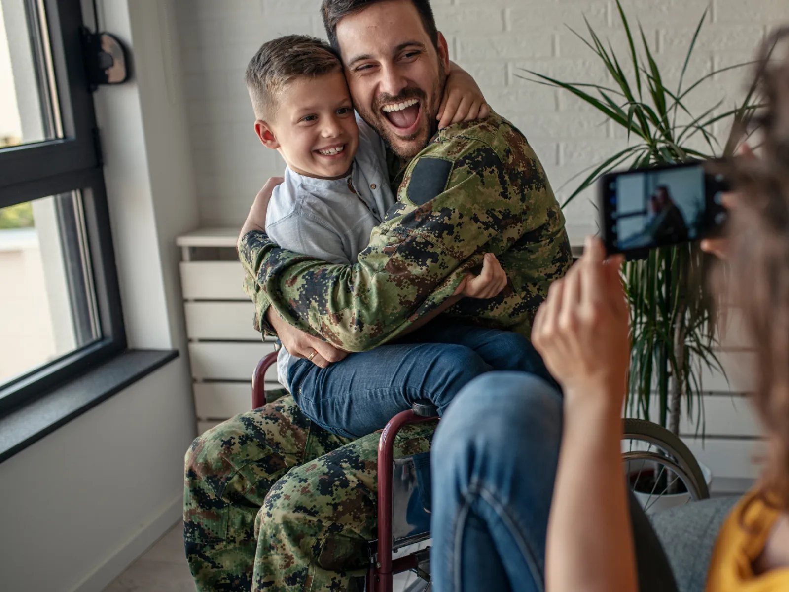 A joyful soldier in uniform embraces his son while being photographed at home.