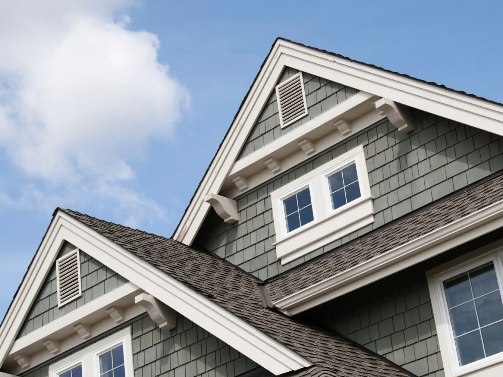 Close-up of a stylish roof with shingles and windows against a clear blue sky.