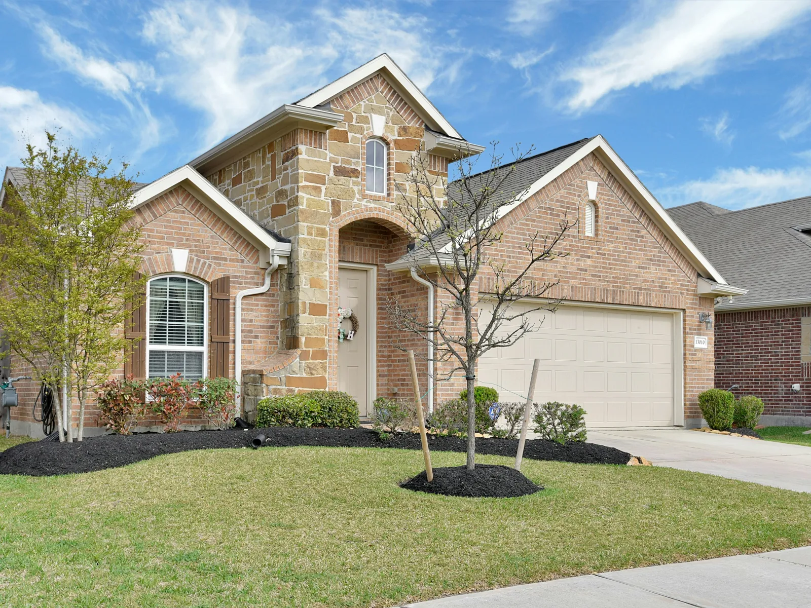 Single-story brick and stone house with a garage, front lawn, and small trees under a blue sky.