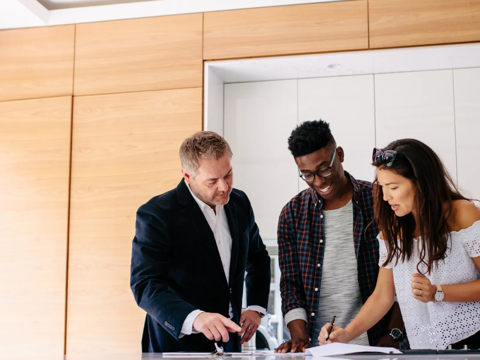 Three people collaborating in a modern kitchen, discussing plans and taking notes.