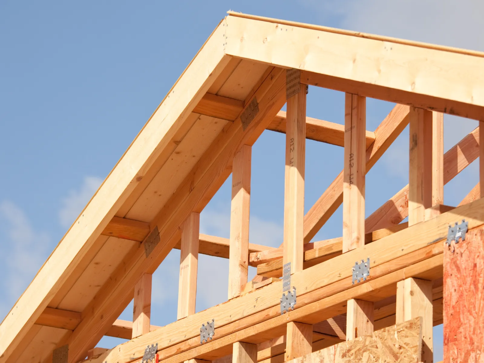Close-up of wooden roof framing under a blue sky, showcasing construction details and craftsmanship.