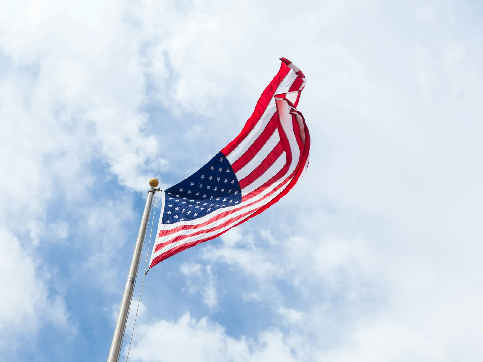 American flag waving against a blue sky with fluffy clouds, symbolizing patriotism and national pride.