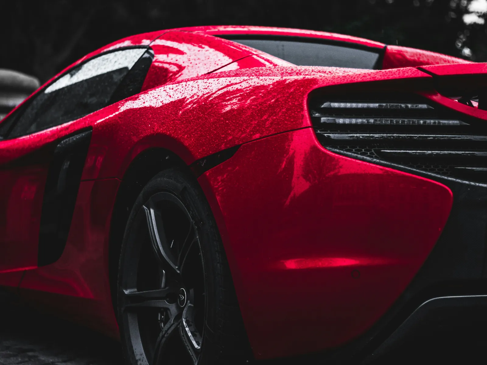 Sleek red sports car glistening with raindrops, showcasing modern design and powerful rear features.