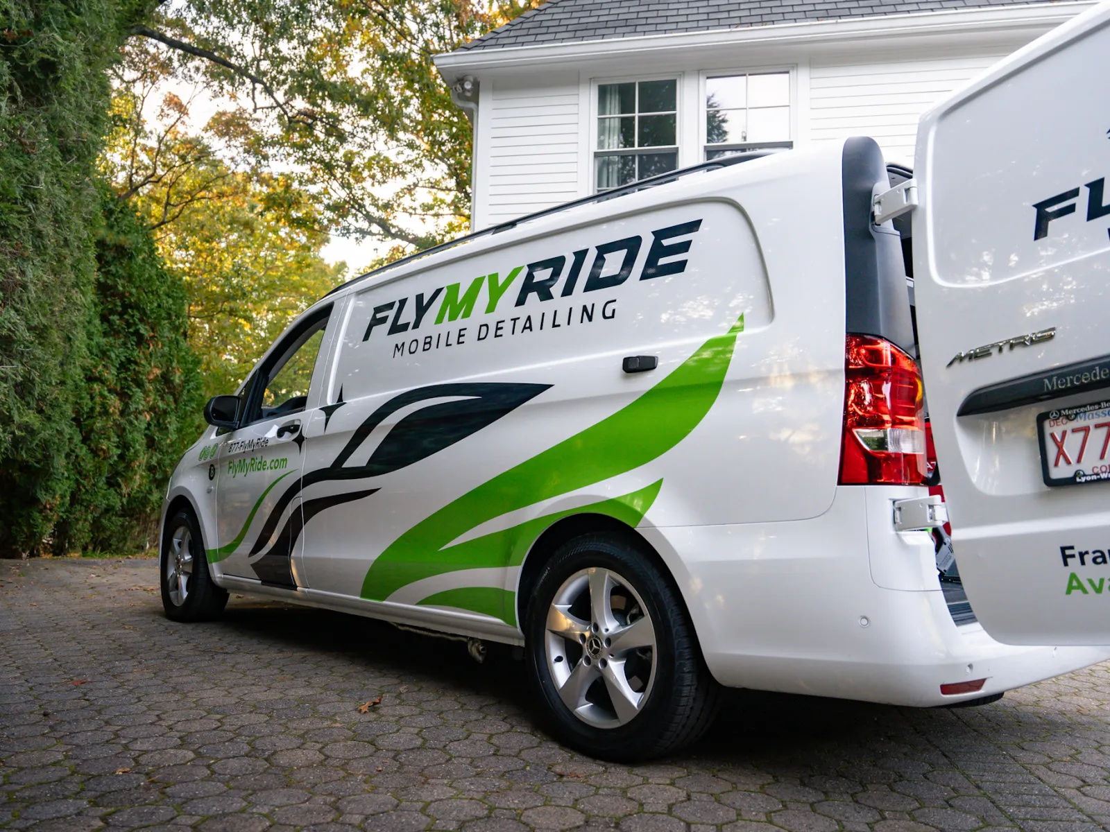 White mobile detailing van with green accents parked in a driveway surrounded by trees.