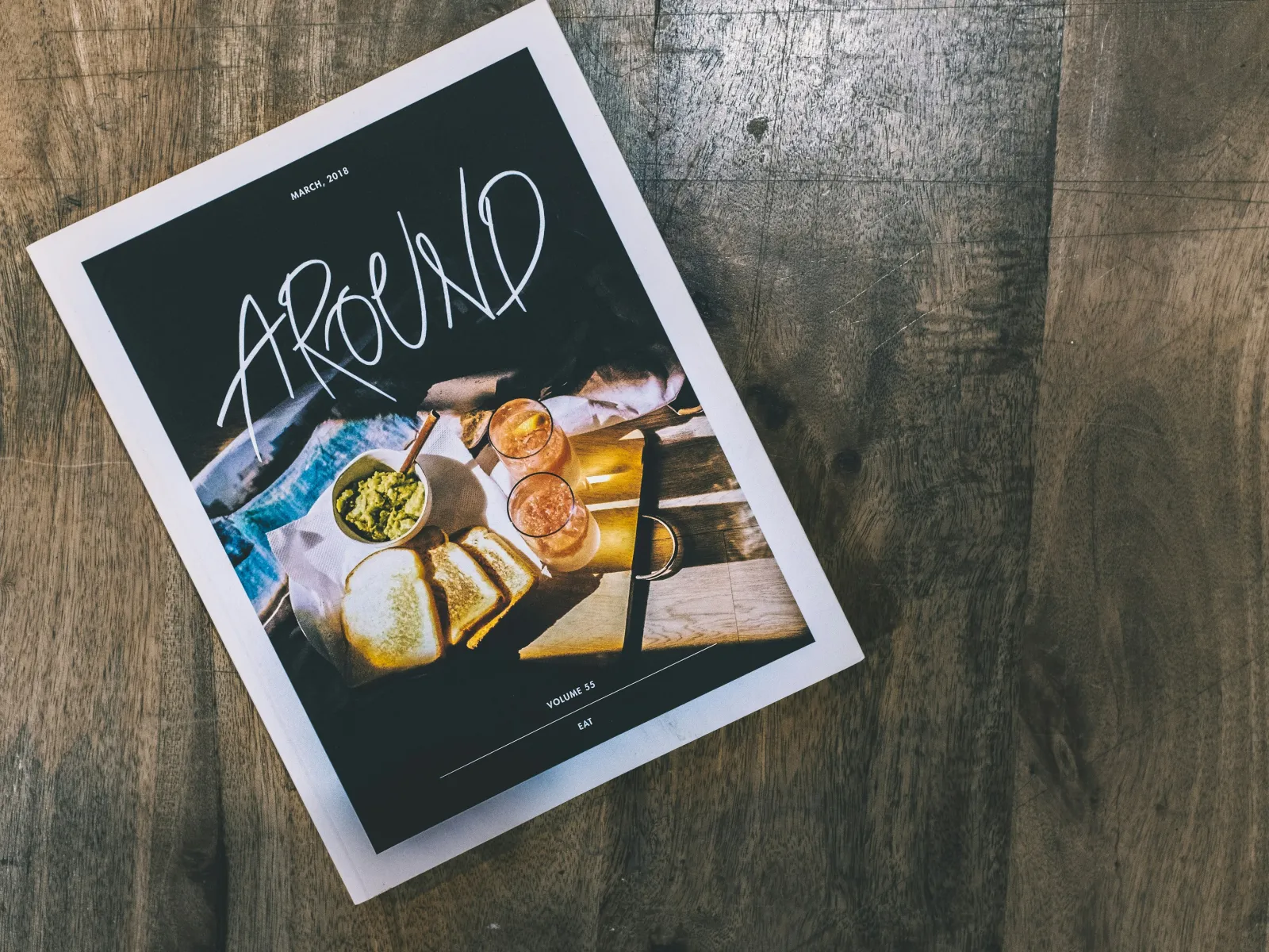 Magazine titled AROUND with food and drinks on cover lying on wooden surface