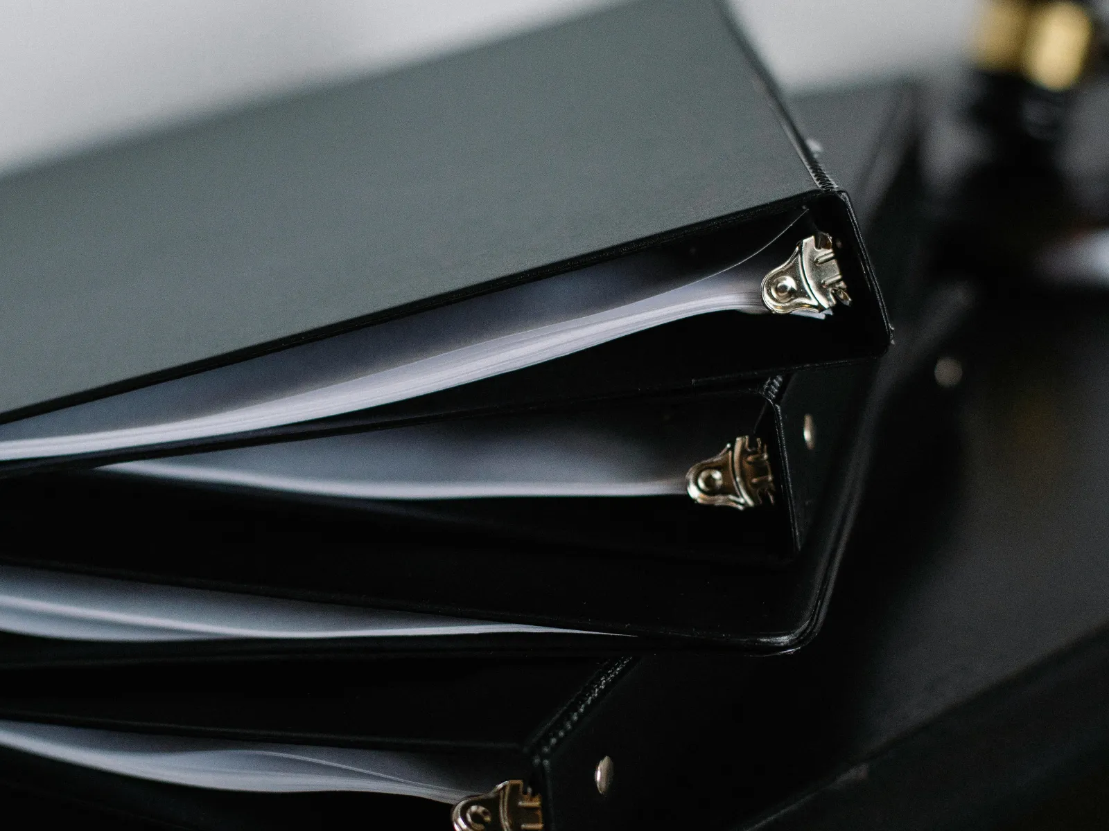 Stack of black binders filled with papers arranged on a dark surface under soft lighting.