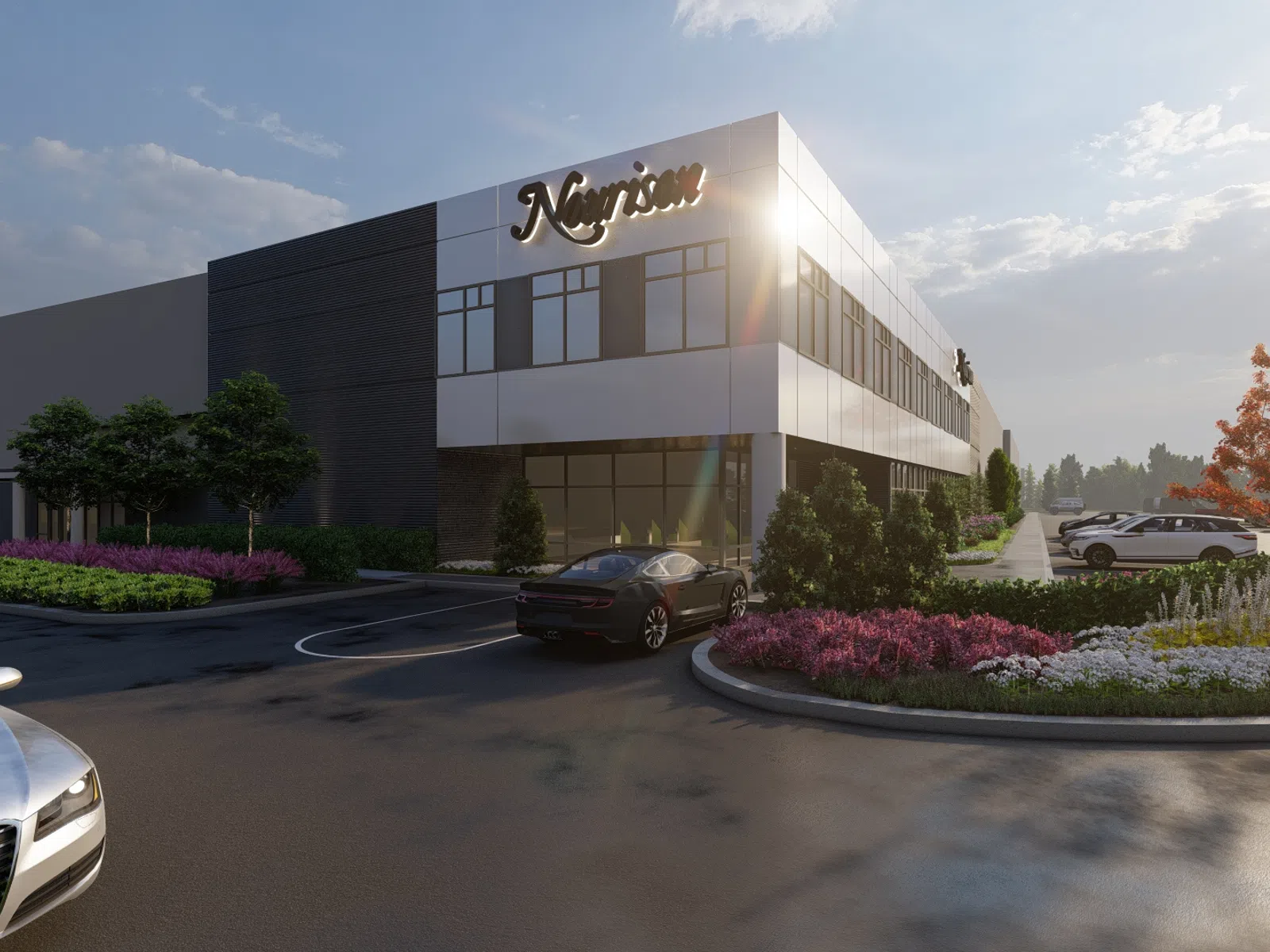 Modern commercial building with landscaped entrance, colorful flowers, and parked cars under a sunny sky.