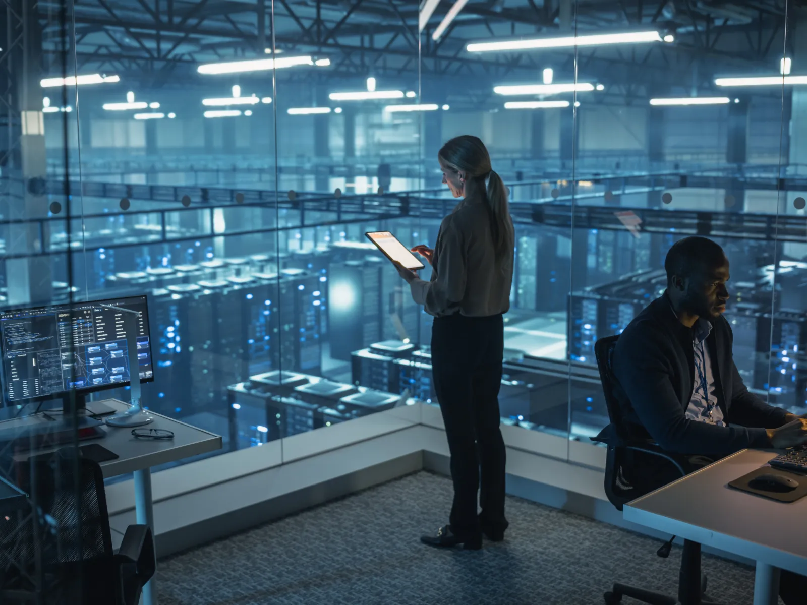 IT professionals working in data center control room with multiple computer screens and servers in the background