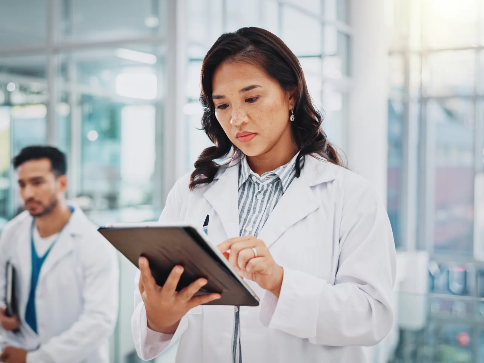 Female doctor using a tablet with a male doctor in the background inside a modern hospital.