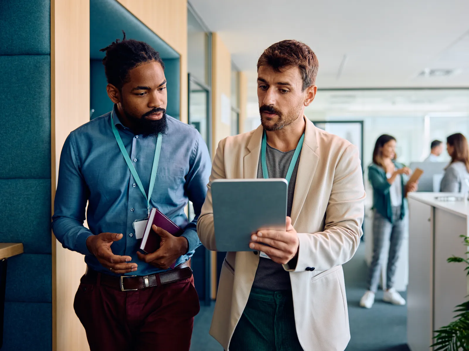 Two businessmen standing and discussing work on a tablet in a modern office environment.