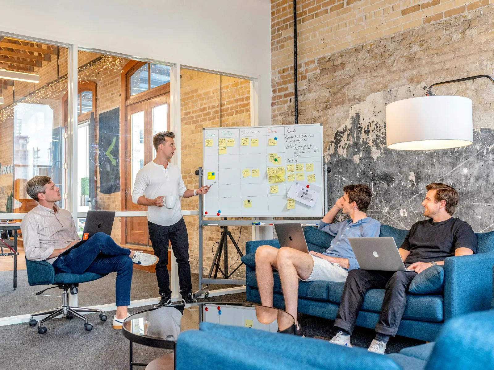 A team collaborates in a modern office, discussing ideas around a whiteboard with laptops.