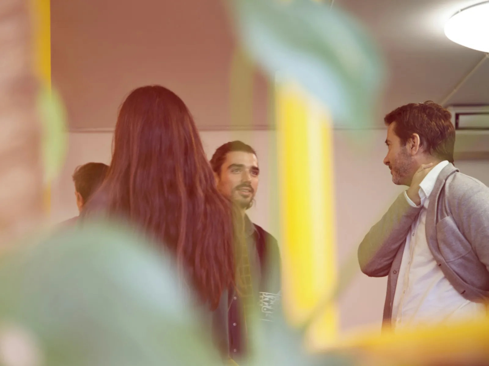 Group of people engaged in conversation in a casual indoor setting surrounded by greenery.