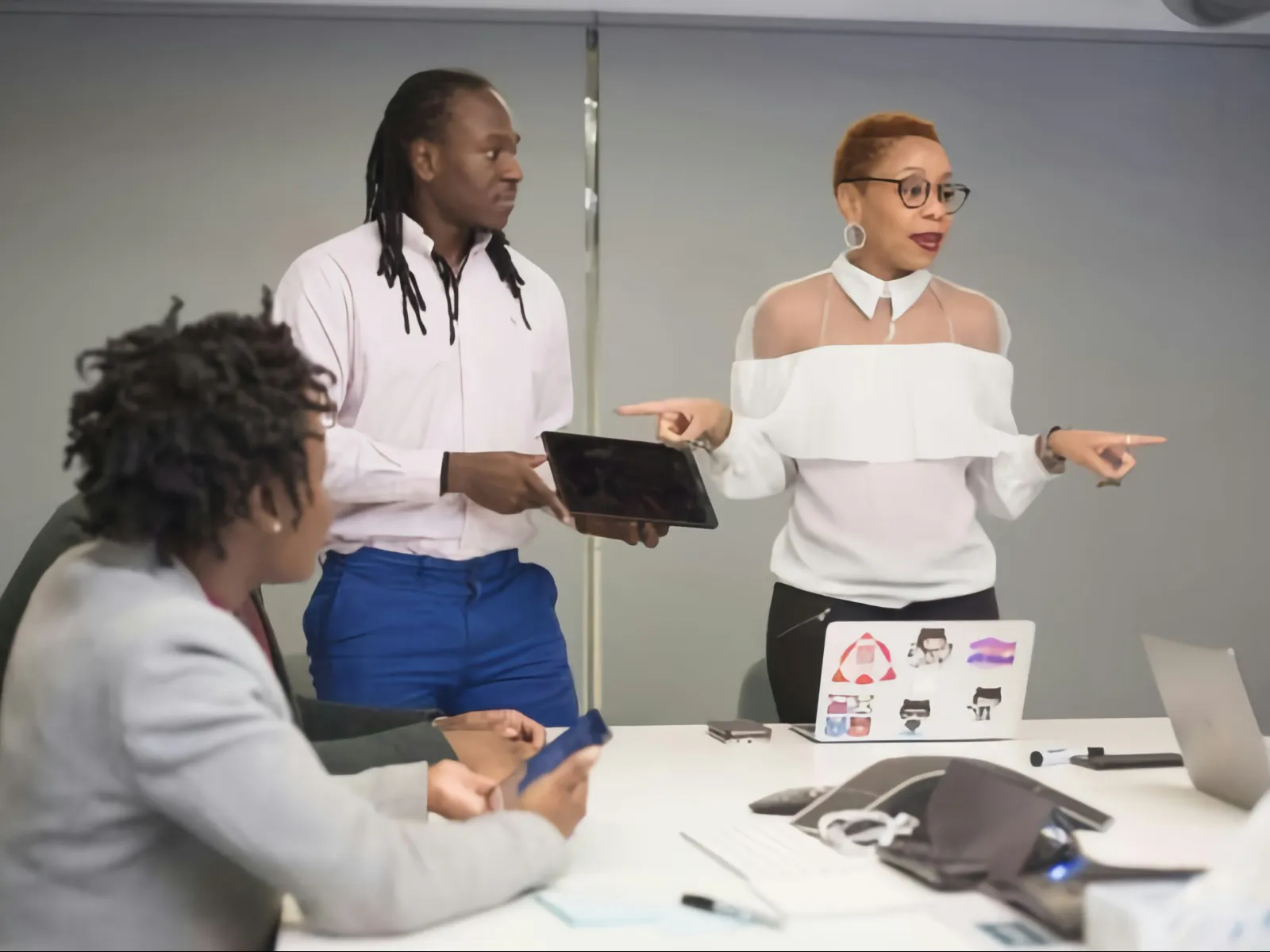 Three business professionals collaborating in a modern office meeting with laptops and tablets at the table.