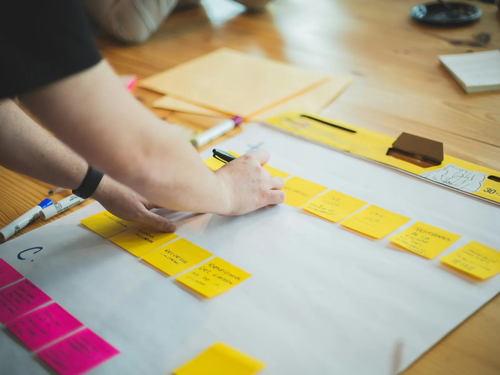 A person writing on sticky notes during a brainstorming session at a table.